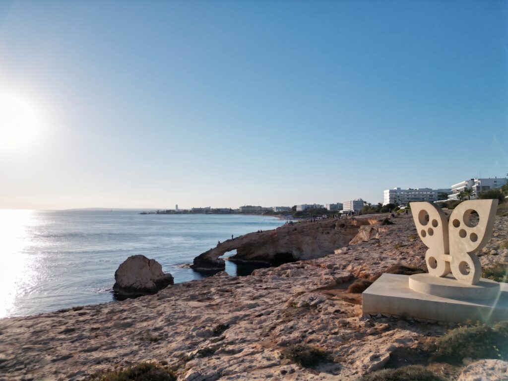A natural sea arch on the Cyprus coast with a sculpture on the headland and the bay beyond