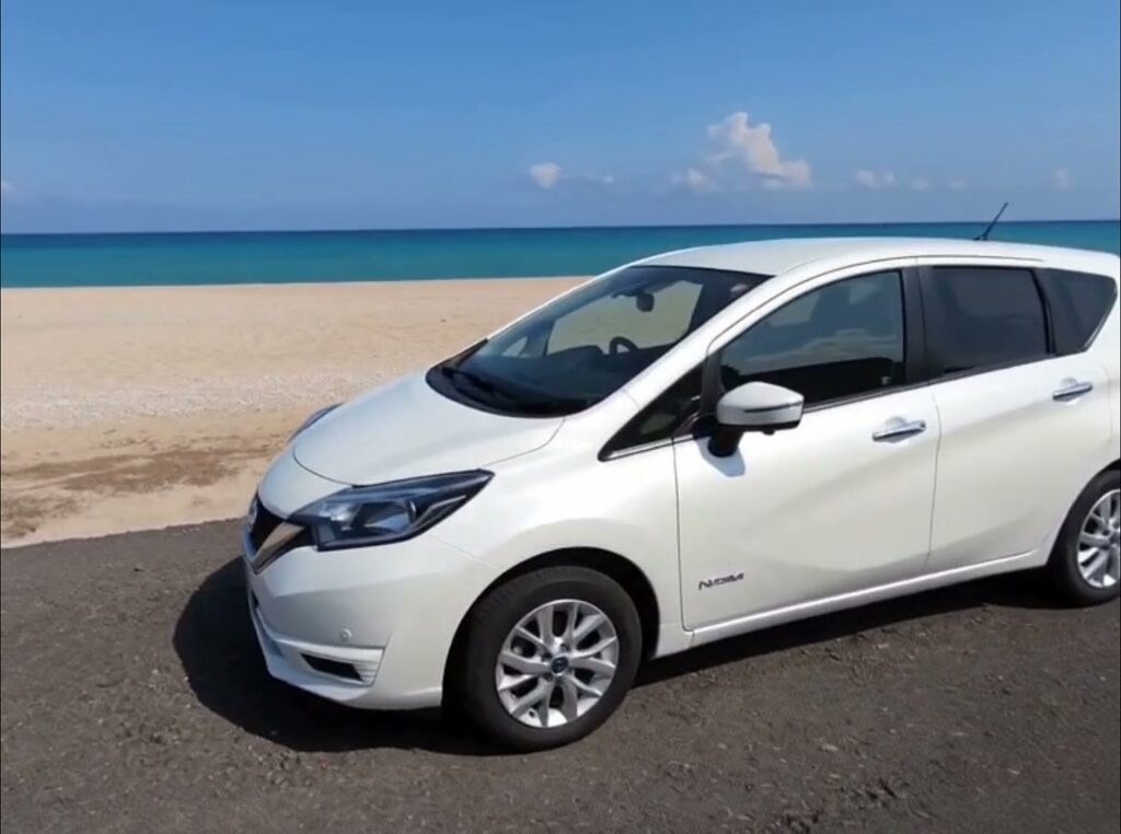 White Nissan Note e-POWER hybrid long-term hire car parked by a beach in Cyprus