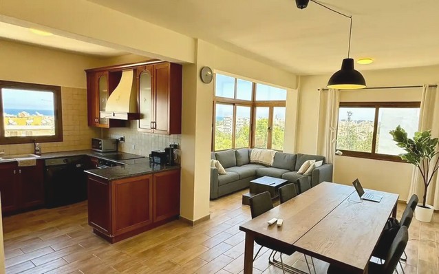Open-plan living and dining area with a large table, sofa and windows looking towards the sea