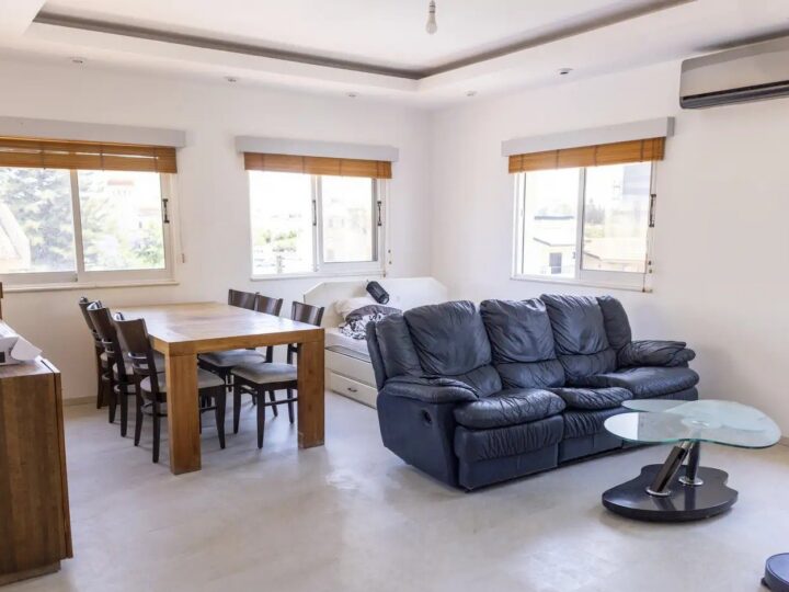 Open living and dining room with sofas, dining table, air conditioning and three windows