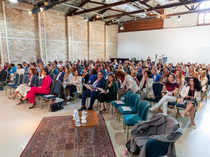 Full audience seated in a stone-walled warehouse venue during a conference session
